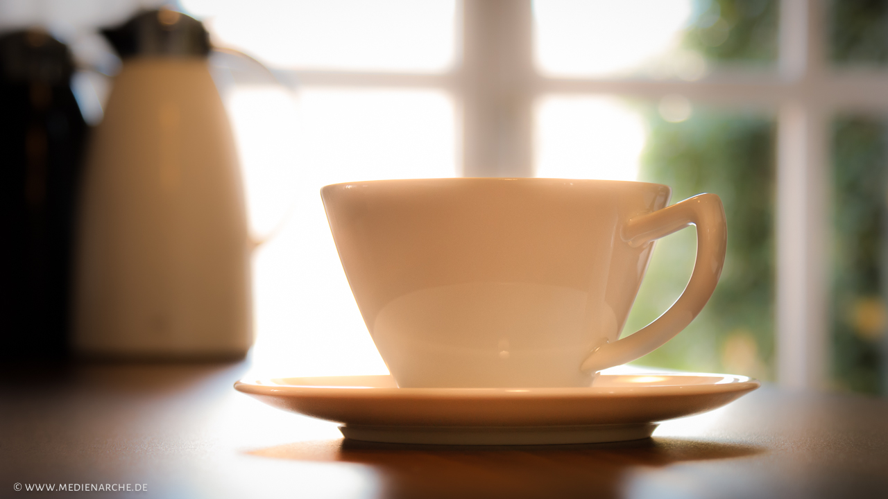 Eine weisse Kaffeetasse vor hell erleuchtetem Fenster